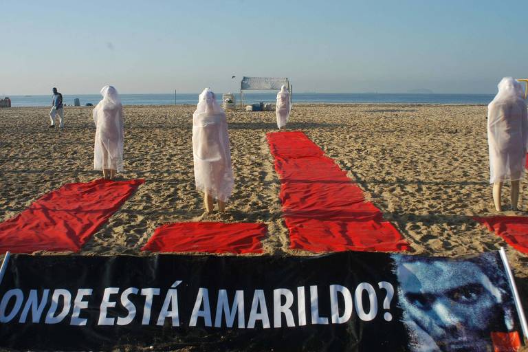Manifestantes cobertos de lençol branco ficam de pé na areia, atrás de uma faixa que diz: "Onde está Amarildo?"