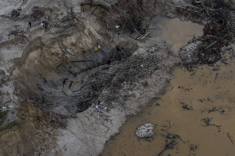 Visão aérea de mineradores trabalhando em uma mina ilegal em Roraima, com as bombas derrubando os barrancos e abrindo ainda mais a cratera