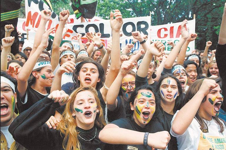 Fotografia colorida mostra jovens vestidos de preto e com rostos pintados de verde amarelo, conhecidos como os caras-pintadas, durante manifestação pelo impeachment do presidente Fernando Collor, em São Paulo