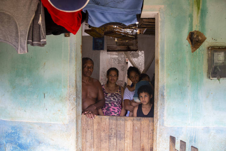 Homem, mulher e crianças dentro de casa muito antiga, com roupas penduradas na varanda