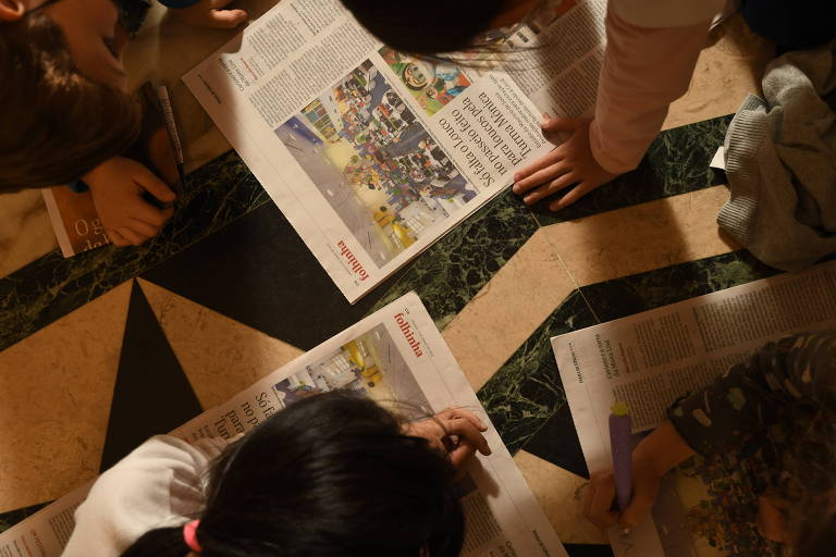 A foto mostra um grupo de crianças lendo edições impressas da Folha.