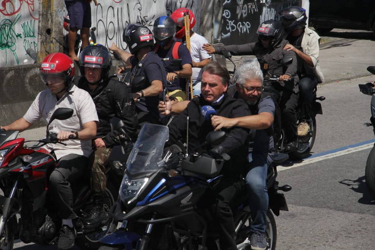 Presidente Jair Bolsonaro anda de moto com um homem grisalho na garupa, ambos estão sem capacete