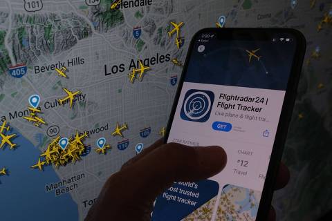 In this illustration photo, the Flightradar24 app is seen on a smartphone in front of a screen showing the live position of planes tracked by the app in the area of Los Angeles, California, on August 5, 2022. - How to upset Russian freight companies, Elon Musk, Chinese authorities and Kylie Jenner in one go? Track their jets. 
Flight following websites and Twitter accounts offer real-time views of air traffic - and sometimes major news like Nancy Pelosi's Taiwan trip - but that exposure draws pushback ranging from complaints to gear seizures. (Photo by Chris Delmas / AFP)