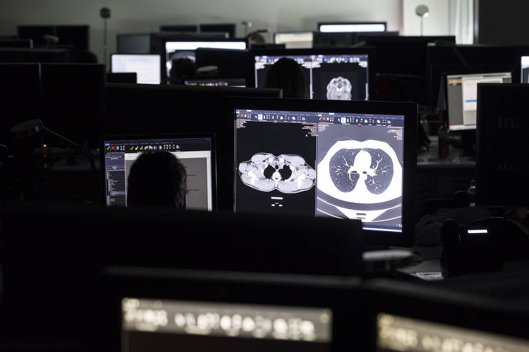 Imagem mostra sala com diversos monitores que exibem exames de imagem de pacientes com câncer
