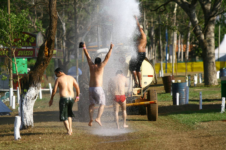Homens pulam em camping na frente de água jogada por caminhão pipa