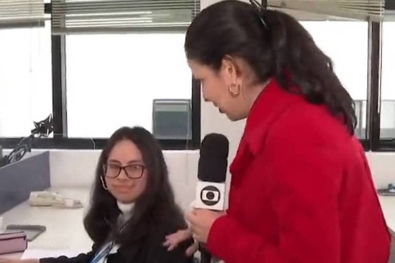 Em foto, jovem sentada em frente ao computador presta a atenção na pergunta de um repórter