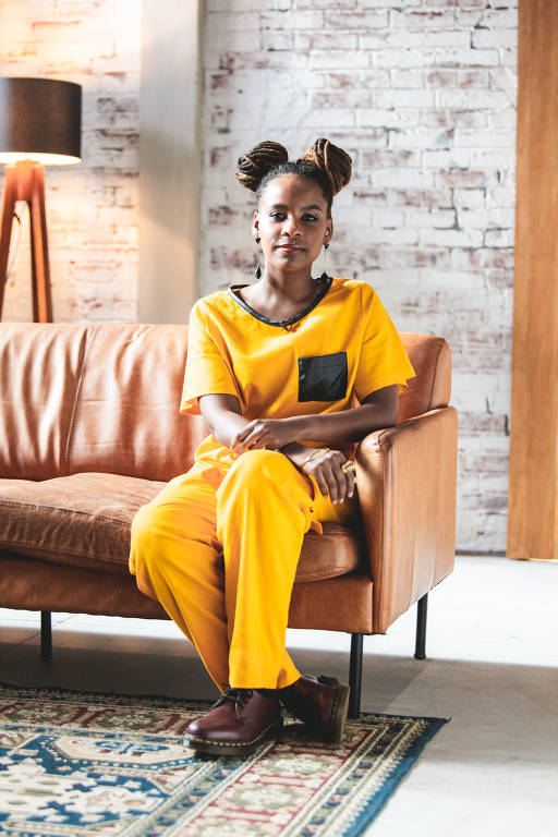 foto de monique evelle, mulher negra que aparece sentada em um sofá e usa roupa amarela