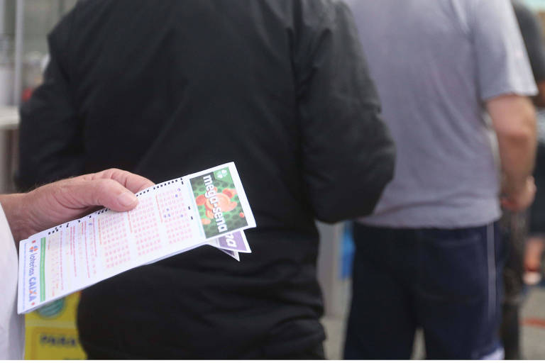 Homem em fila de apostas na lotérica com um boleto de mega-sena na mão