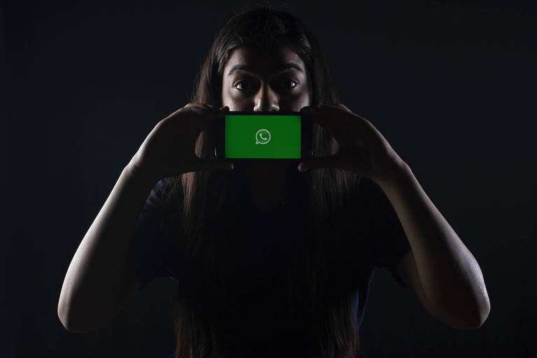 Mulher segura sobre a boca um celular com o logotipo do WhatsApp