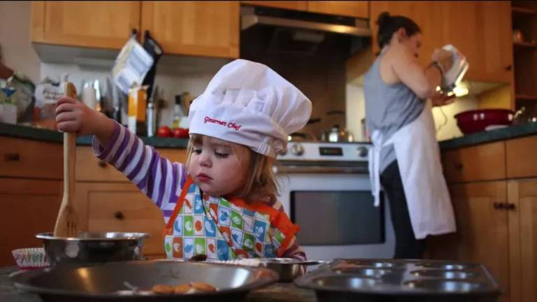 Criança, com chapéu de cozinheiro, mexe numa panela com colher de pau