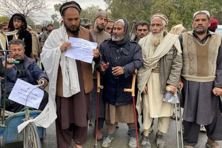 homem segura placa, cercado por outros afegãos