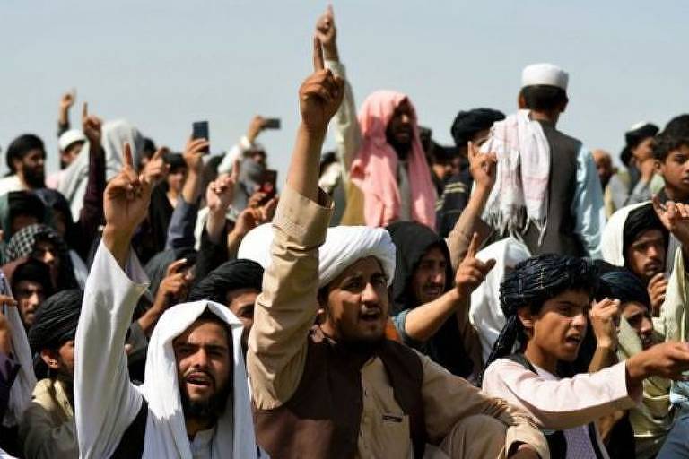 homens afegãos levantam as mãos, em ambiente aberto, sob sol apino