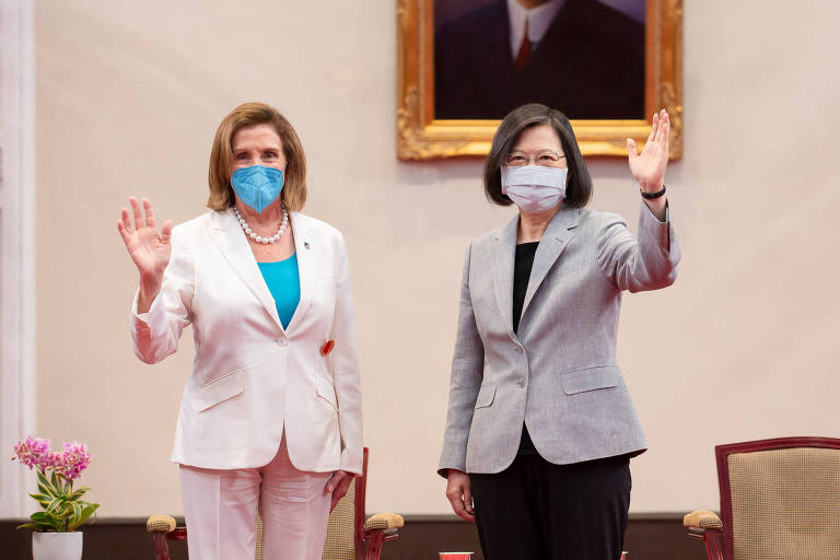 A presidente da Câmara dos Deputados dos EUA, Nancy Pelosi (esq.), e a presidente de Taiwan, Tsai Ing-wen, durante a visita da congressista a Taiwan; as duas estão de pé, usam máscara de proteção contra a Covid e acenam com uma das mãos no momento da foto
