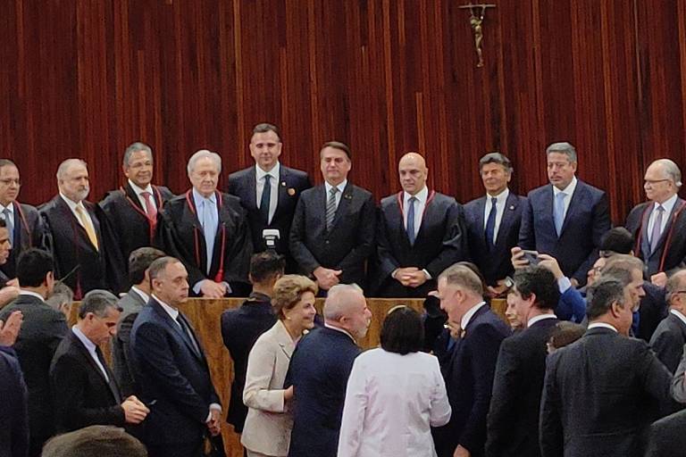 Imagem mostra Bolsonaro ao centro, ao lado de Alexandre de Moraes e outros ministros; ele olha para Lula e Dilma, que estão à frente