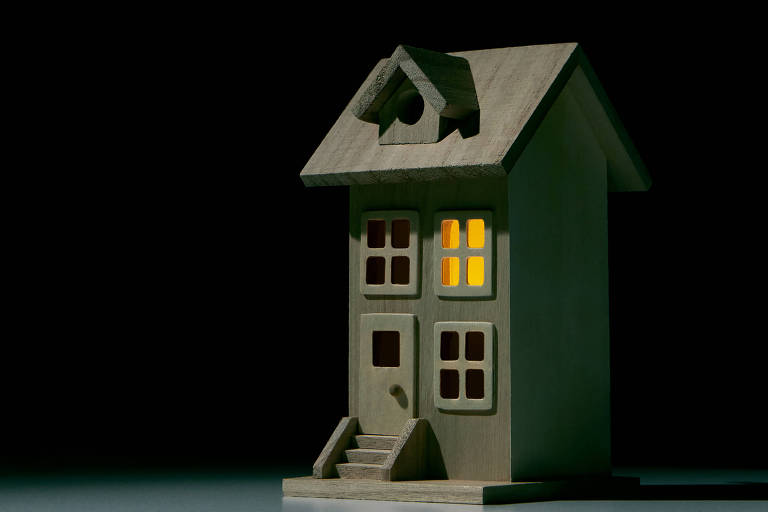 Uma casa de duas janelas uma porta com escada em um fundo escuro. Uma janela está com a luz acesa