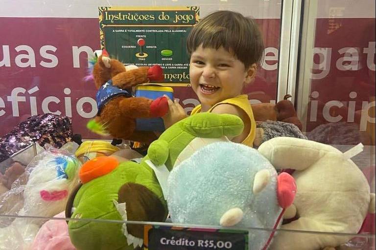 Em foto colorida, menino entra na máquina de pegar bichinhos de pelúcia