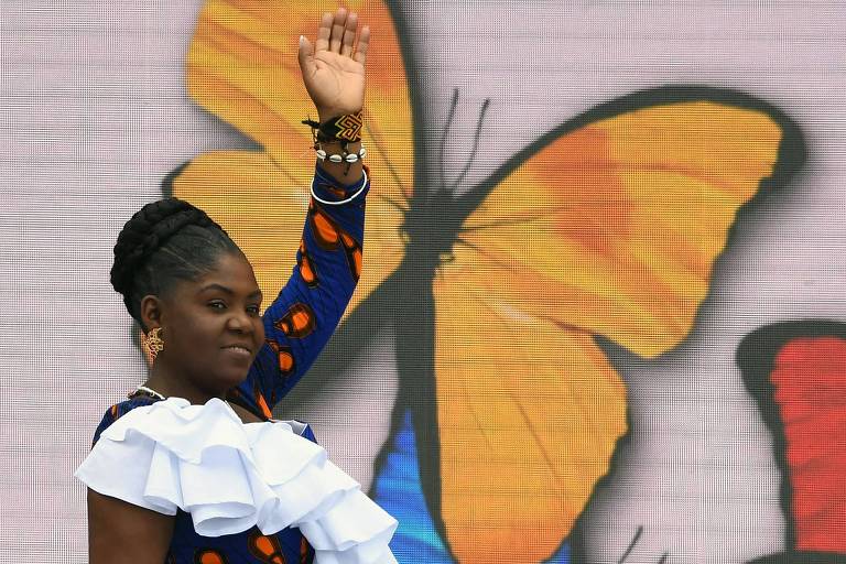 A vice-presidente da Colômbia, Francia Márquez, acena com a mão esquerda erguida em evento na capital do país, Bogotá; atrás dela há um painel em que aparece uma grande borboleta na cor laranja 