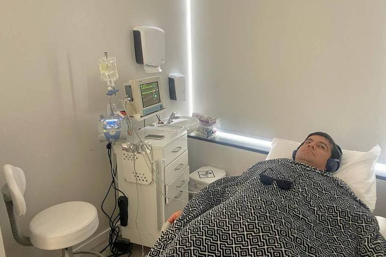 Homem deitado em cama hospitalar rodeado de equipamentos médicos