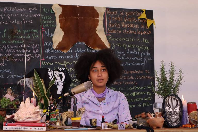 A autora Adriele Oliveira no centro de uma mesa com um quadro-negro atrás