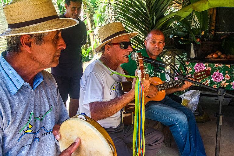 Em foto colorida, participantes de um dos grupos folclóricos aparecem tocando seus instrumentos