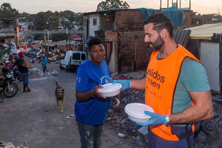 Voluntário entrega marmita em ação da ONG Unidos do Bem, no Morro do Piolho, em São Paulo