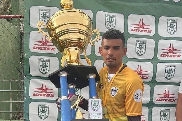 Em foto colorida, homem com uniforme de futebol ergue uma taça