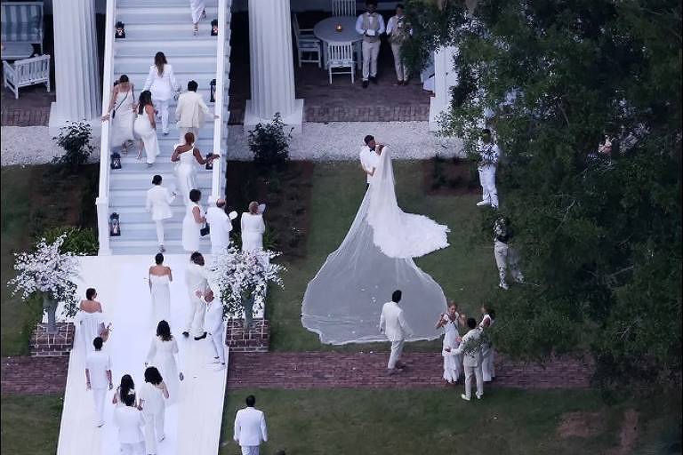 Em foto colorida tirada do alto, noivos se beijam diante dos convidados