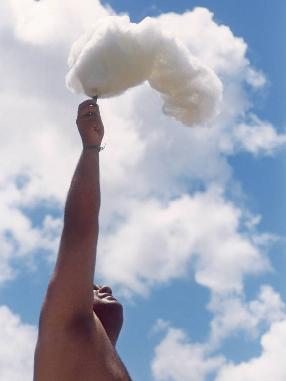 homem segura algodão doce contra as nuvens de dia ensolarado