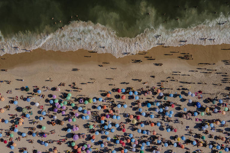 Vista aérea da areia, com multidão em guarda-sóis