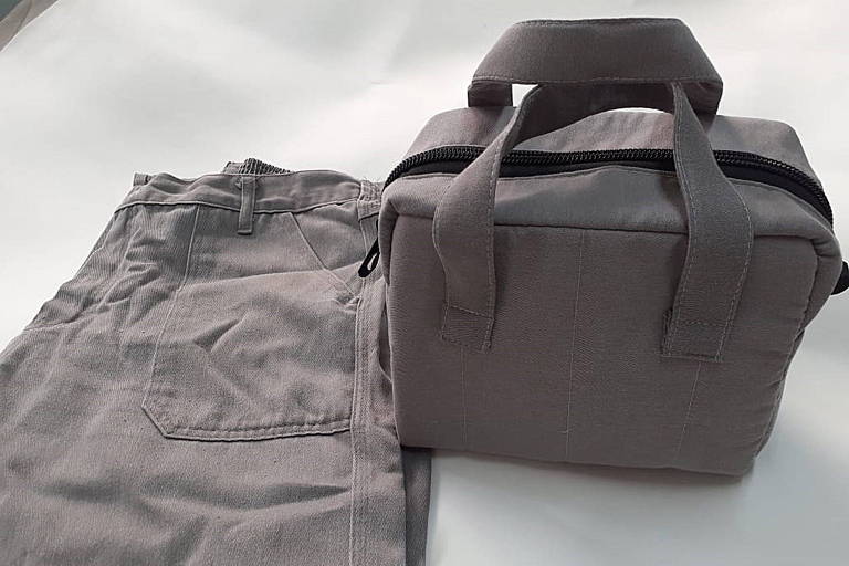 Imagem colorida mostra uma calça cinza dobrada; à direita, uma bolsa no mesmo tom da cor da calça