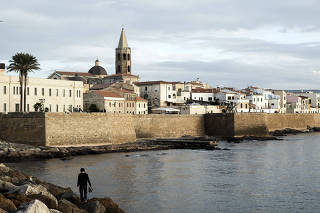 On the coast of Alghero with the bell tower for the Cathedral of Santa Maria visible in the historic port in Sardinia.
