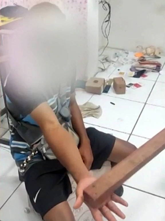 trecho de vídeo mostra homem sentado com rosto oculto com maos abertas e pedaço de madeira batendo na palma
