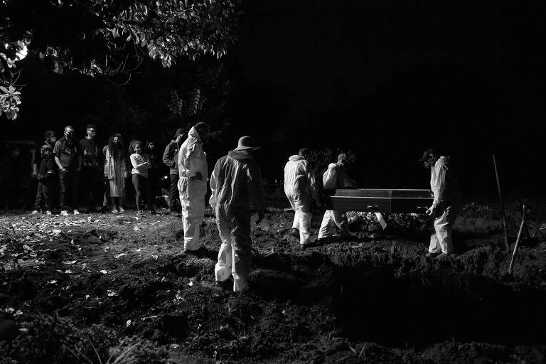Pessoas com roupas de proteção carregam caixão no meio da escuridão