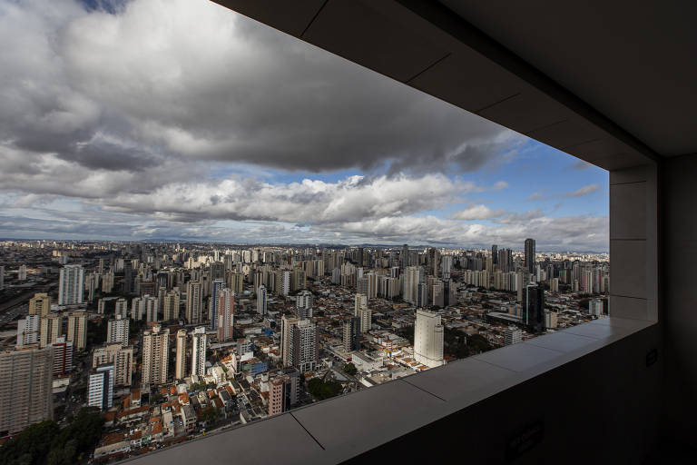 a foto, tirada do alto de um prédio, mostra a vista de um bairro urbanizado abaixo. destacam-se os vários prédios menores e um céu carregado de nuvens