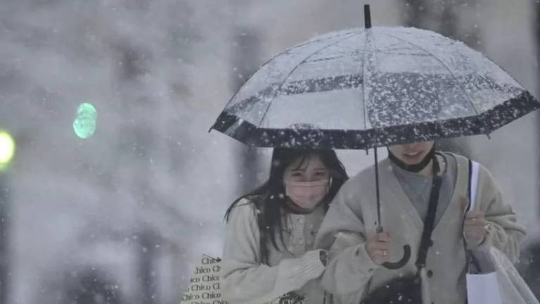 Duas mulheres andam na chuva embaixo de apenas um guarda-chuva