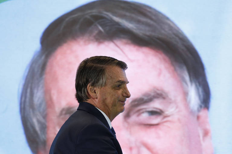 O presidente bolsonaro passa em frente a uma foto de seu rosto em tamanho gigante
