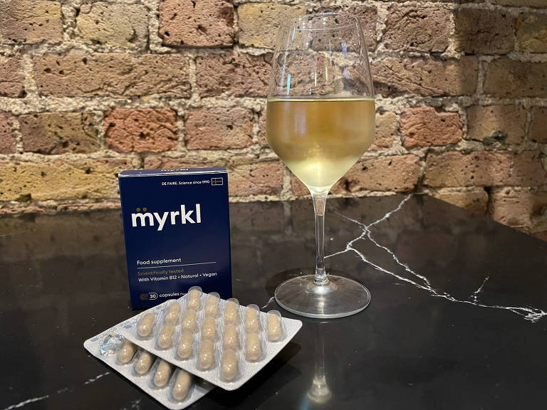 Caixa do produto Myrkl, pílula que promete acabar com a ressaca, em uma mesa ao lado de uma taça de vinho