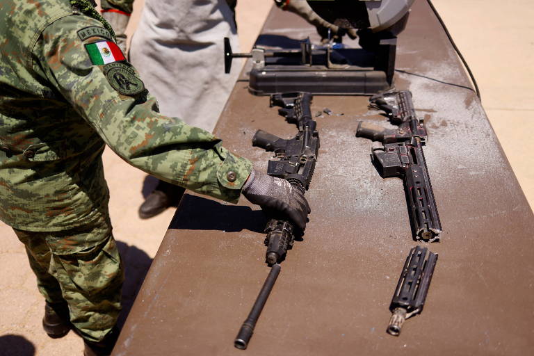 Militar mexicano coloca a mão direita sobre um fuzil que está sobre uma mesa durante cerimônia na base de Ciudad Juarez na qual foram destruídas armas apreendidas do crime organizado