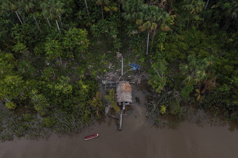 Vista de drone de uma casa com placas solares no quintal; no entorno há rio e árvores