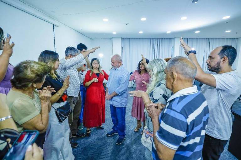 O ex-presidente Lula aparece rodeado de pessoas, que estendem os braços em posição de oraçãoendem 