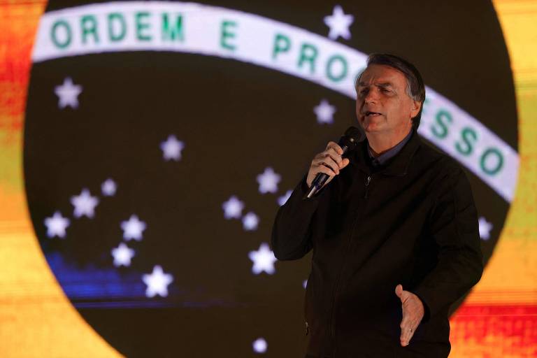 Bolsonaro gesticula em frente à imagem de uma bandeira do Brasil