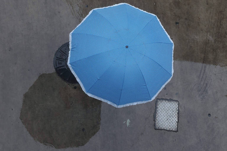 Foto tirado do alto, mostrando um guarda-chuva azul cobrindo uma pessoa que caminha no Viaduto do Chá, em São Paulo.