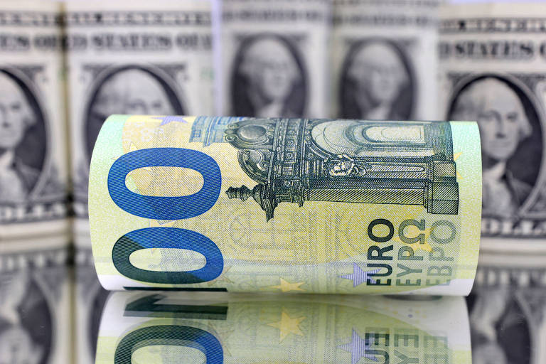 Nota de euro enrolada e tombada diante de notas de dólar americano