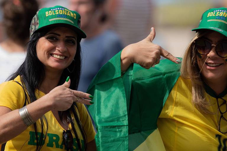 Mulheres com camiseta do Brasil fazem sinal de arma com as mãos