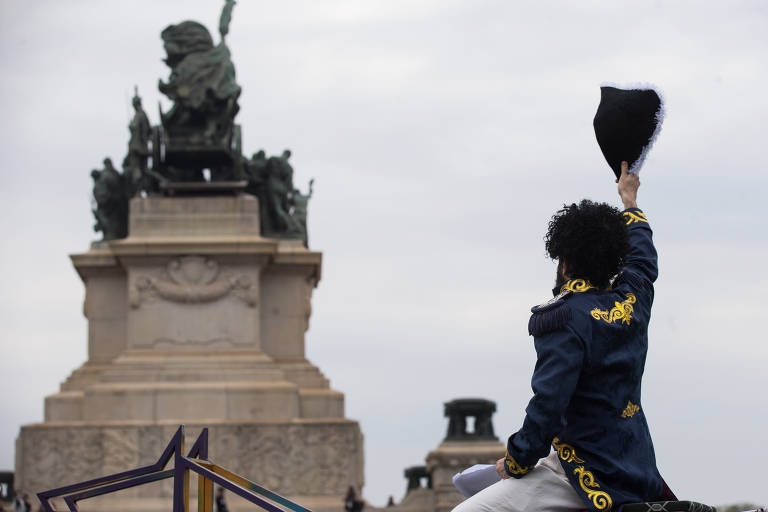 Fantasiado com farda de dom Pedro 1º, Caco Ciocler levanta um chapéu em aceno ao Monumento da Independência