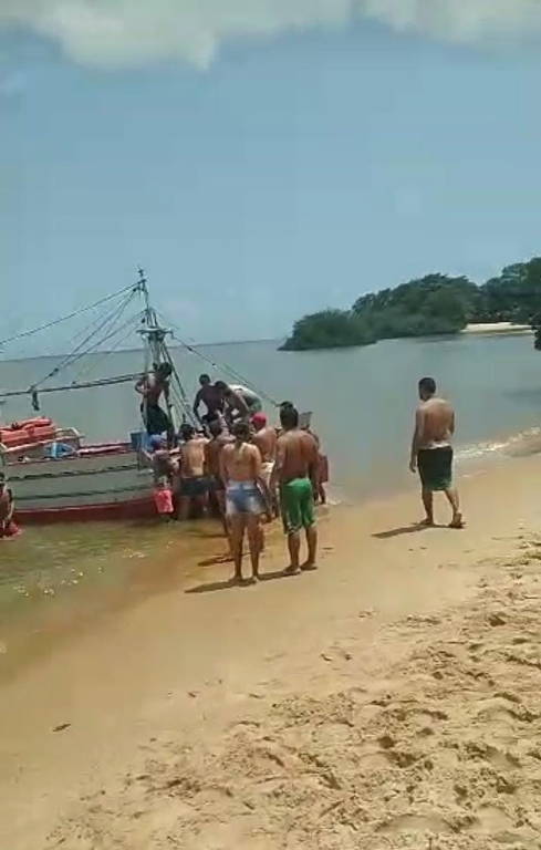 Um grupo de pessoas está na areia, à beira de uma praia, perto de um barco