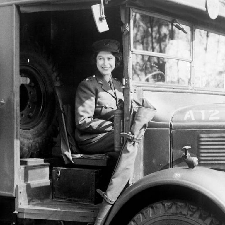 Foto em preto e branco mostra uma mulher dentro de uma carro militar; ela usa uma farda, chapéu e sorri para a foto