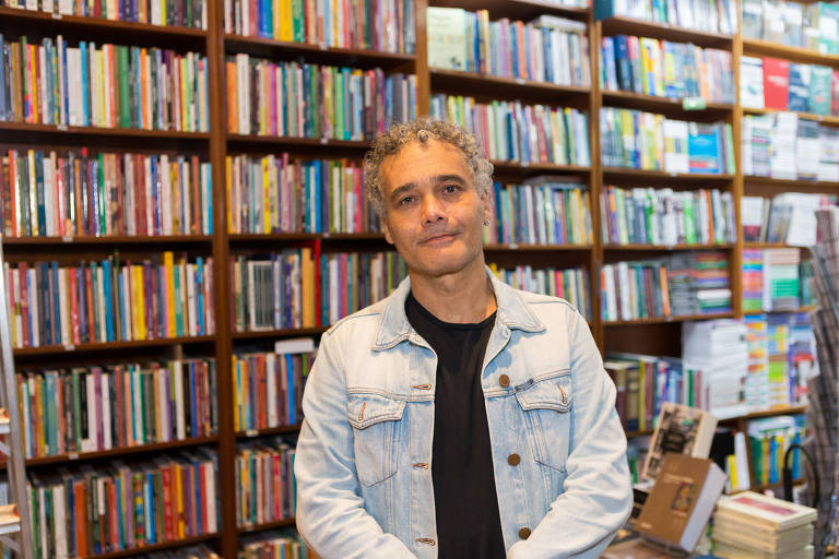 Escritor Sidarta Ribeiro em pé em frente a uma estante de livros