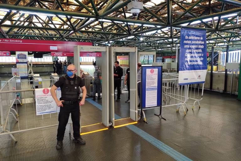 Um segurança do metrô em frente a dois detectores de metal de corpo inteiro nas catracas da estação Dom Pedro 2º