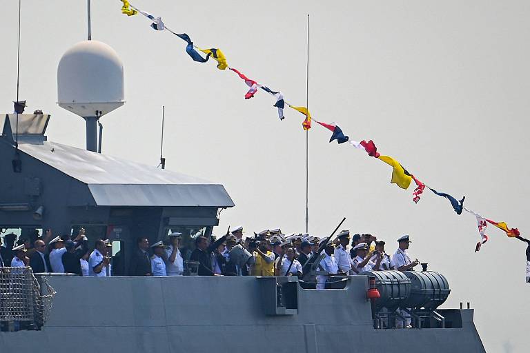 O presidente Jair Bolsonaro acena enquanto navega em um navio de guerra brasileiro durante cerimônia militar da Marinha, na Baía de Guanabara, no Rio de Janeiro, neste sábado (10).